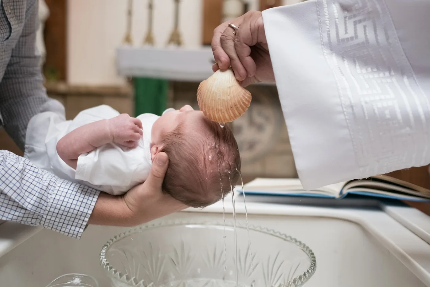 Sacerdote bautizando a un bebé con agua sobre la pila bautismal